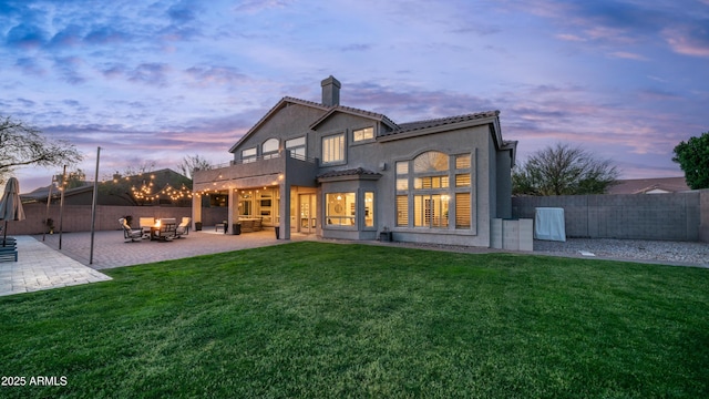 rear view of house with fence, a chimney, stucco siding, a patio area, and a lawn