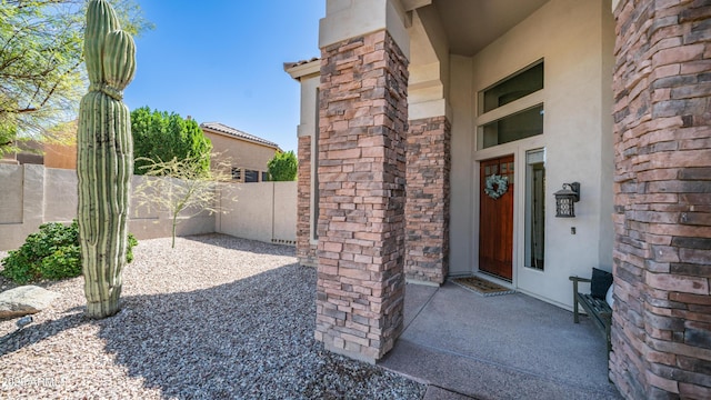 property entrance featuring a patio area, fence, stone siding, and stucco siding