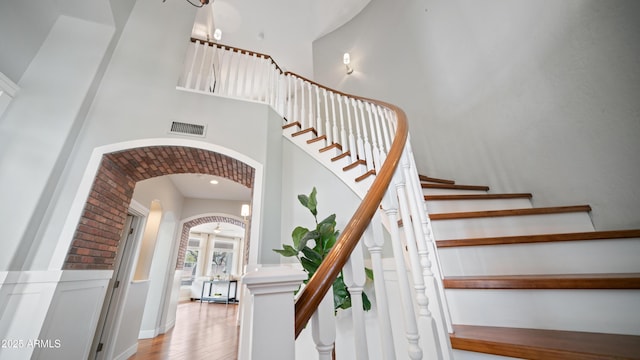 stairway with visible vents, a wainscoted wall, a towering ceiling, wood finished floors, and arched walkways