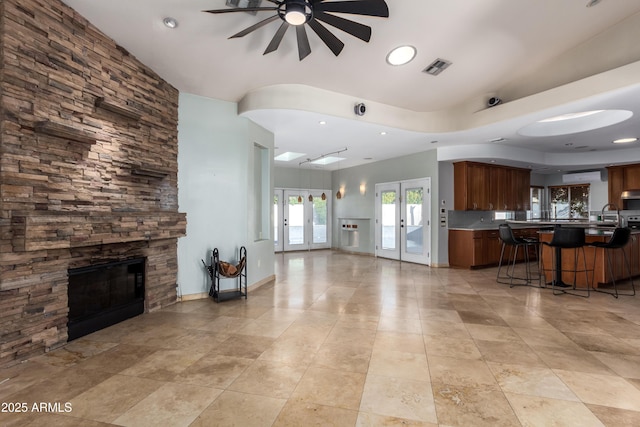 unfurnished living room featuring ceiling fan, french doors, sink, and a fireplace