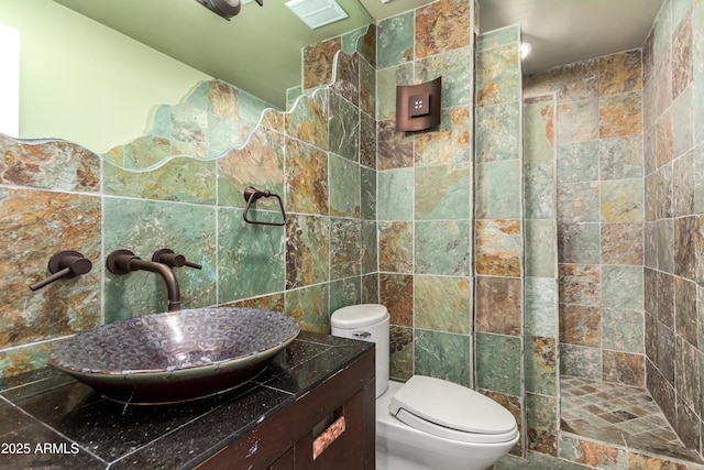 bathroom featuring tile walls, a tile shower, vanity, and toilet