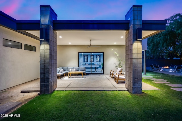 rear view of property featuring a lawn, an outdoor living space with a fire pit, a ceiling fan, and a patio area