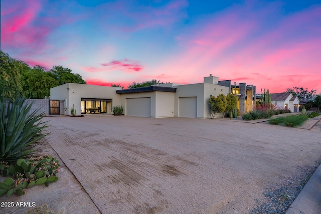 modern home with a garage, dirt driveway, and stucco siding