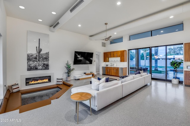 living room with a glass covered fireplace, a towering ceiling, recessed lighting, and visible vents