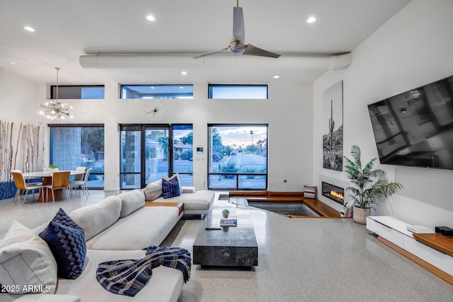 living area featuring recessed lighting, a glass covered fireplace, ceiling fan with notable chandelier, and a towering ceiling