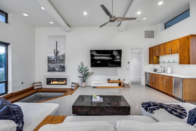 living room with a ceiling fan, visible vents, light speckled floor, a glass covered fireplace, and a high ceiling