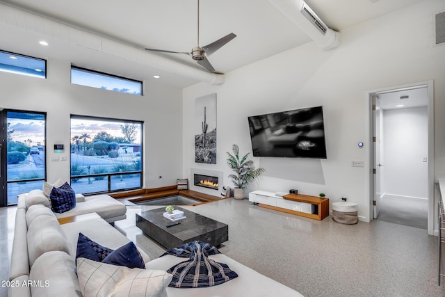 living area with ceiling fan, visible vents, a towering ceiling, baseboards, and a glass covered fireplace