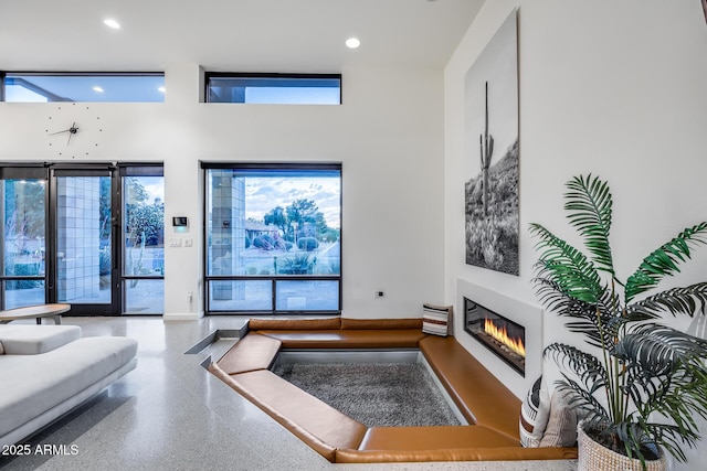 living room with recessed lighting, a glass covered fireplace, speckled floor, and a towering ceiling