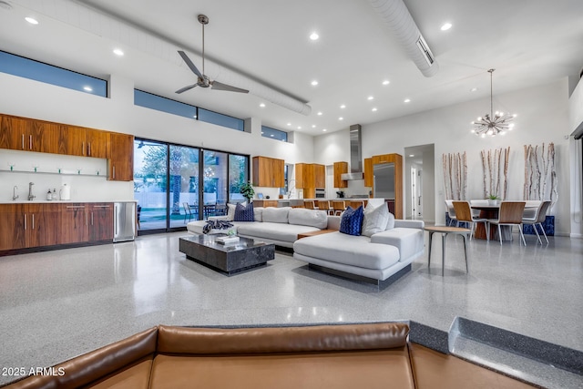 living area with ceiling fan with notable chandelier, recessed lighting, speckled floor, and a towering ceiling