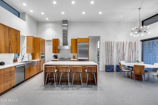 kitchen featuring wall chimney range hood, brown cabinetry, appliances with stainless steel finishes, modern cabinets, and a sink