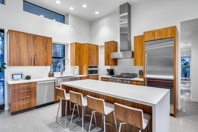 kitchen with modern cabinets, a high ceiling, wall chimney range hood, and stainless steel appliances