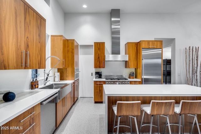 kitchen featuring modern cabinets, wall chimney exhaust hood, brown cabinets, a sink, and stainless steel appliances