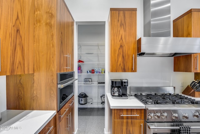 kitchen with stainless steel range with gas stovetop, modern cabinets, brown cabinets, and wall chimney range hood