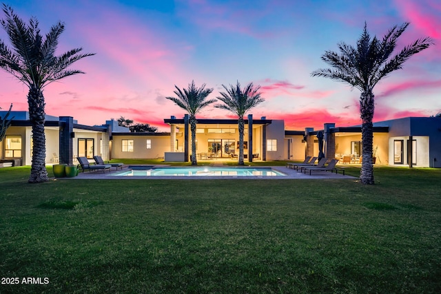 back of house at dusk featuring a lawn, a patio, an outdoor pool, and stucco siding