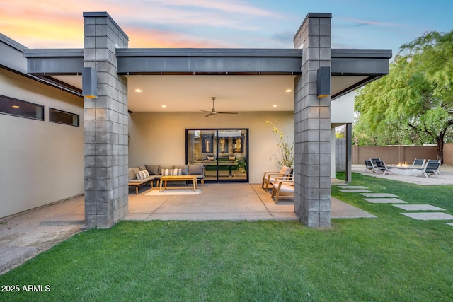 back of property at dusk with a chimney, a ceiling fan, a patio area, an outdoor living space with a fire pit, and a yard