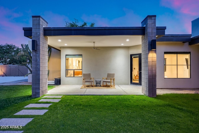 back of property at dusk featuring a lawn, a patio area, and stucco siding