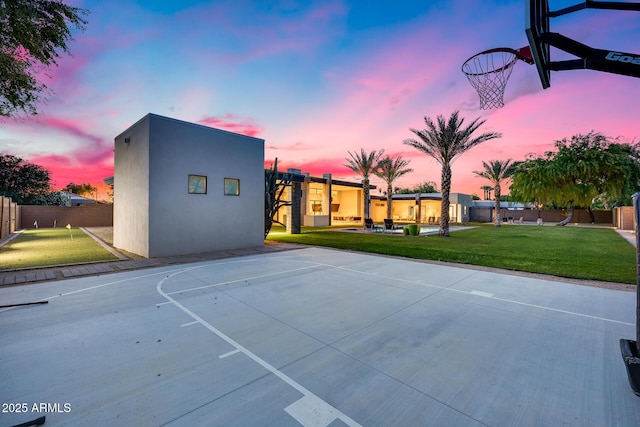 view of basketball court with fence, a yard, and basketball hoop