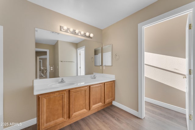 full bath featuring double vanity, visible vents, wood finished floors, a sink, and baseboards