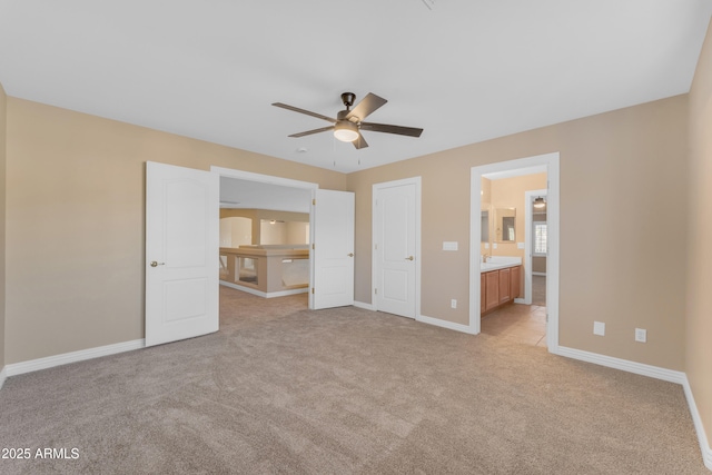unfurnished bedroom with baseboards, a ceiling fan, ensuite bath, and light colored carpet