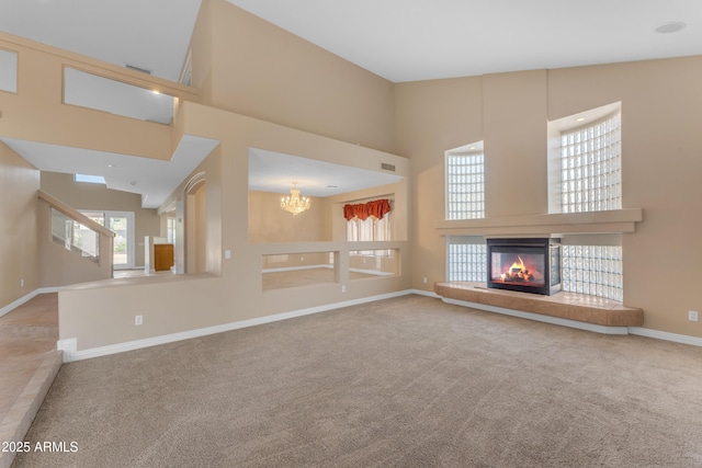 unfurnished living room featuring a notable chandelier, carpet, a multi sided fireplace, baseboards, and a towering ceiling