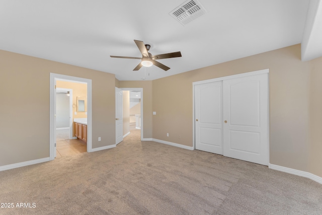 unfurnished bedroom with visible vents, a closet, baseboards, light colored carpet, and ensuite bath