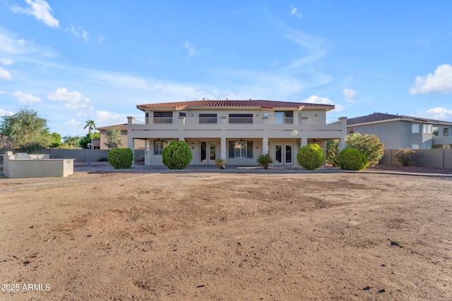 view of front of house with a tiled roof, fence, french doors, and a balcony