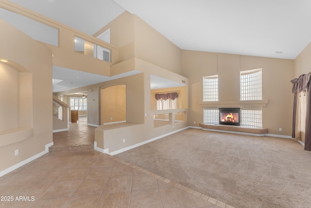 unfurnished living room featuring a glass covered fireplace, tile patterned flooring, a high ceiling, and baseboards