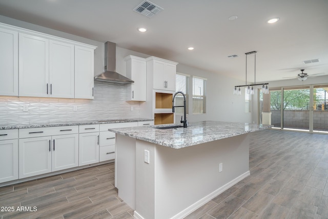 kitchen with white cabinetry, sink, wall chimney exhaust hood, and a kitchen island with sink