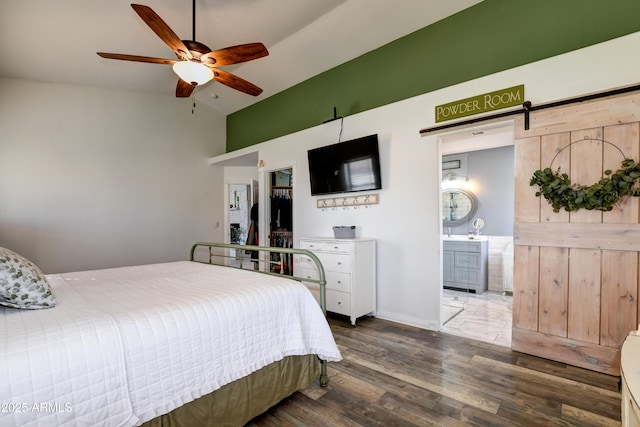 bedroom with a barn door, connected bathroom, vaulted ceiling, ceiling fan, and wood finished floors