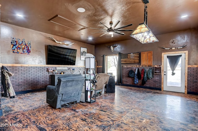 living area with attic access, ceiling fan, and brick wall