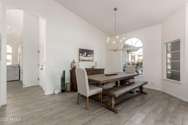 dining area featuring light hardwood / wood-style flooring, high vaulted ceiling, and an inviting chandelier