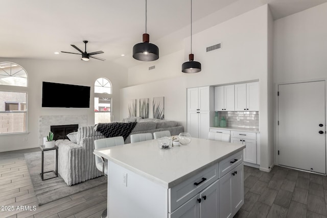 kitchen featuring a stone fireplace, a center island, white cabinets, and hanging light fixtures