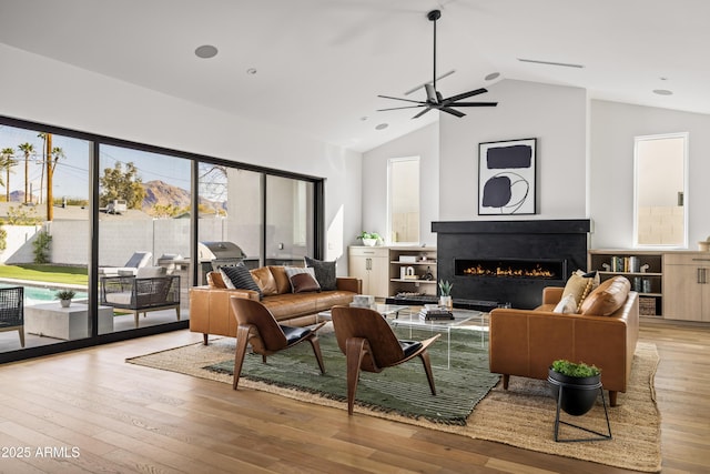 living area with lofted ceiling, a ceiling fan, wood-type flooring, and a lit fireplace