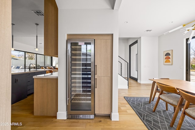 wine area with beverage cooler, baseboards, visible vents, light wood finished floors, and a sink