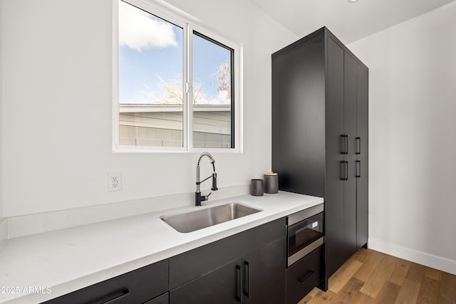 kitchen featuring light wood finished floors, a sink, stainless steel microwave, light countertops, and dark cabinets