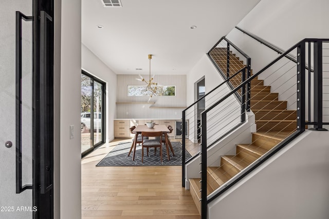 dining space with visible vents, wood-type flooring, an inviting chandelier, and stairs