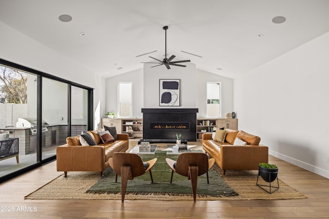 living room featuring hardwood / wood-style floors, a ceiling fan, baseboards, a lit fireplace, and vaulted ceiling