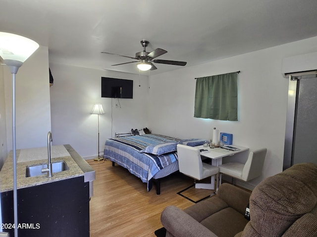 bedroom with a wall unit AC, sink, ceiling fan, and light hardwood / wood-style flooring