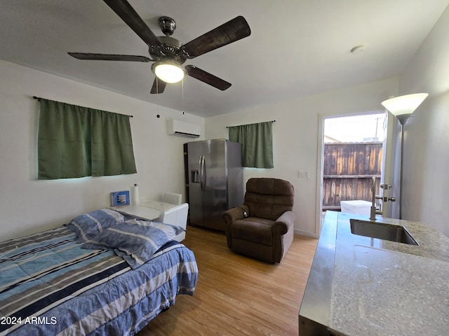 bedroom featuring sink, a wall unit AC, stainless steel refrigerator with ice dispenser, ceiling fan, and wood-type flooring