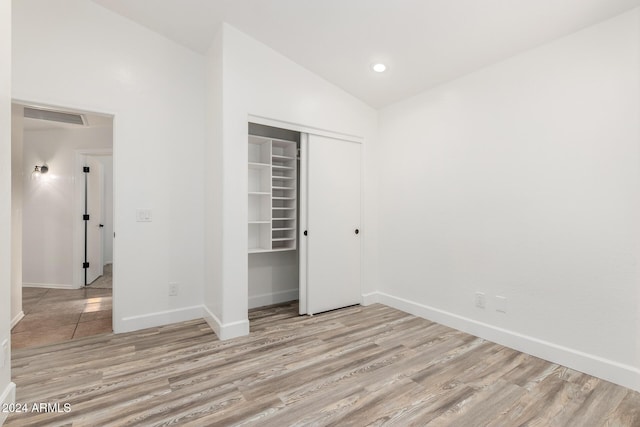 unfurnished bedroom with vaulted ceiling, a closet, and light hardwood / wood-style flooring