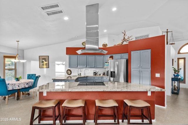 kitchen featuring a breakfast bar, vaulted ceiling, stainless steel refrigerator with ice dispenser, and light stone countertops