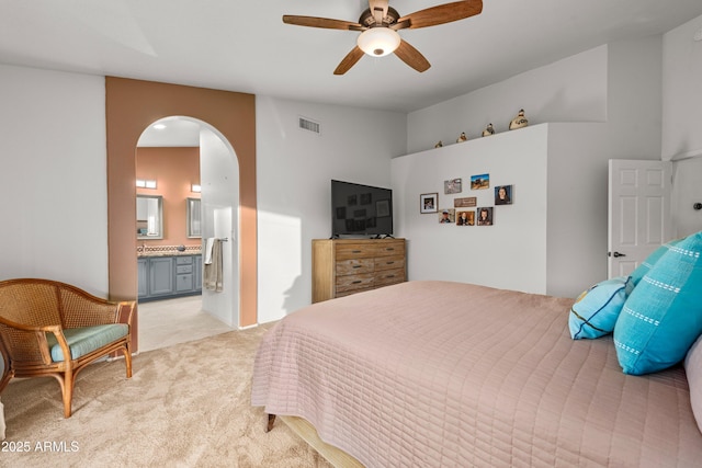 bedroom with arched walkways, light colored carpet, visible vents, a ceiling fan, and ensuite bath