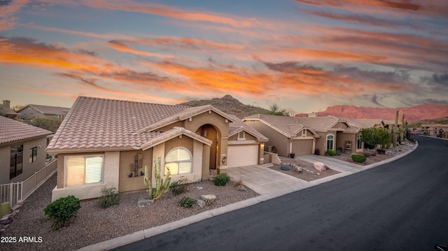 mediterranean / spanish house with driveway, a garage, a tiled roof, a mountain view, and stucco siding