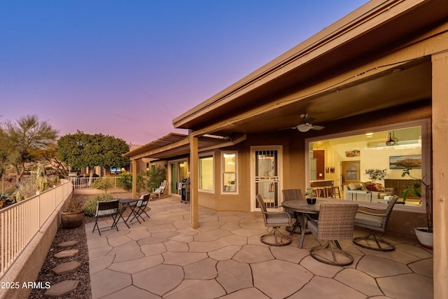 patio terrace at dusk with outdoor dining area, a fenced backyard, and ceiling fan