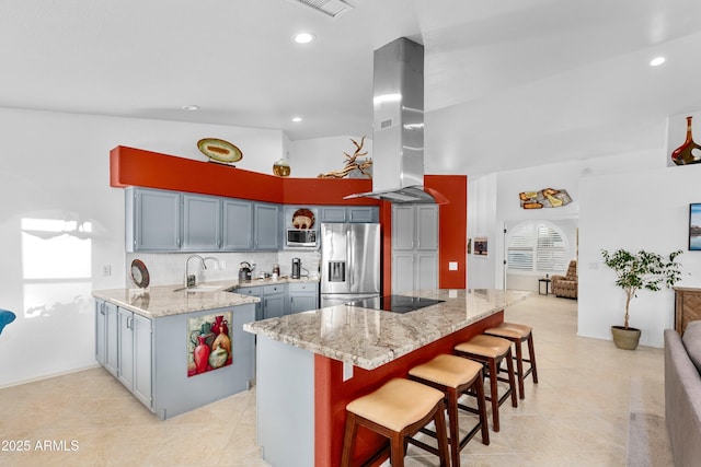 kitchen featuring island exhaust hood, light stone counters, a peninsula, appliances with stainless steel finishes, and a kitchen bar