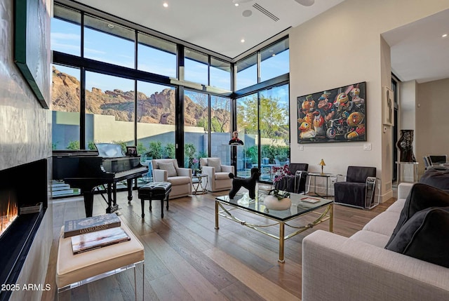 living area featuring visible vents, wood finished floors, a high ceiling, a wall of windows, and a high end fireplace