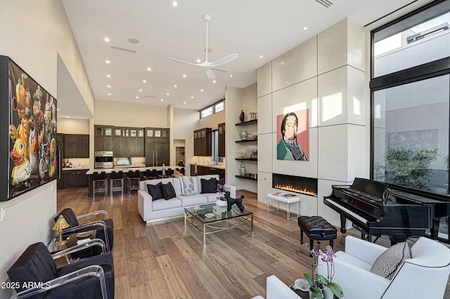 living room with visible vents, wood finished floors, a high ceiling, a fireplace, and recessed lighting