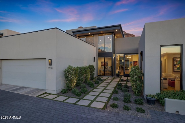 back of property at dusk featuring an attached garage and stucco siding