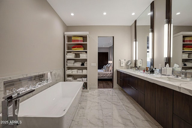 ensuite bathroom with double vanity, connected bathroom, marble finish floor, a freestanding tub, and a sink