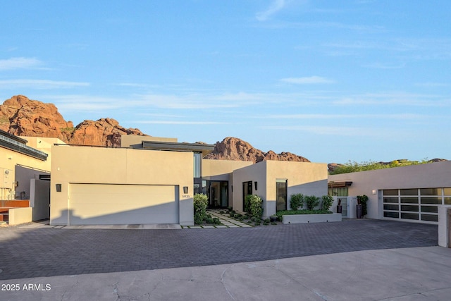 view of front facade with a garage, a mountain view, decorative driveway, and stucco siding